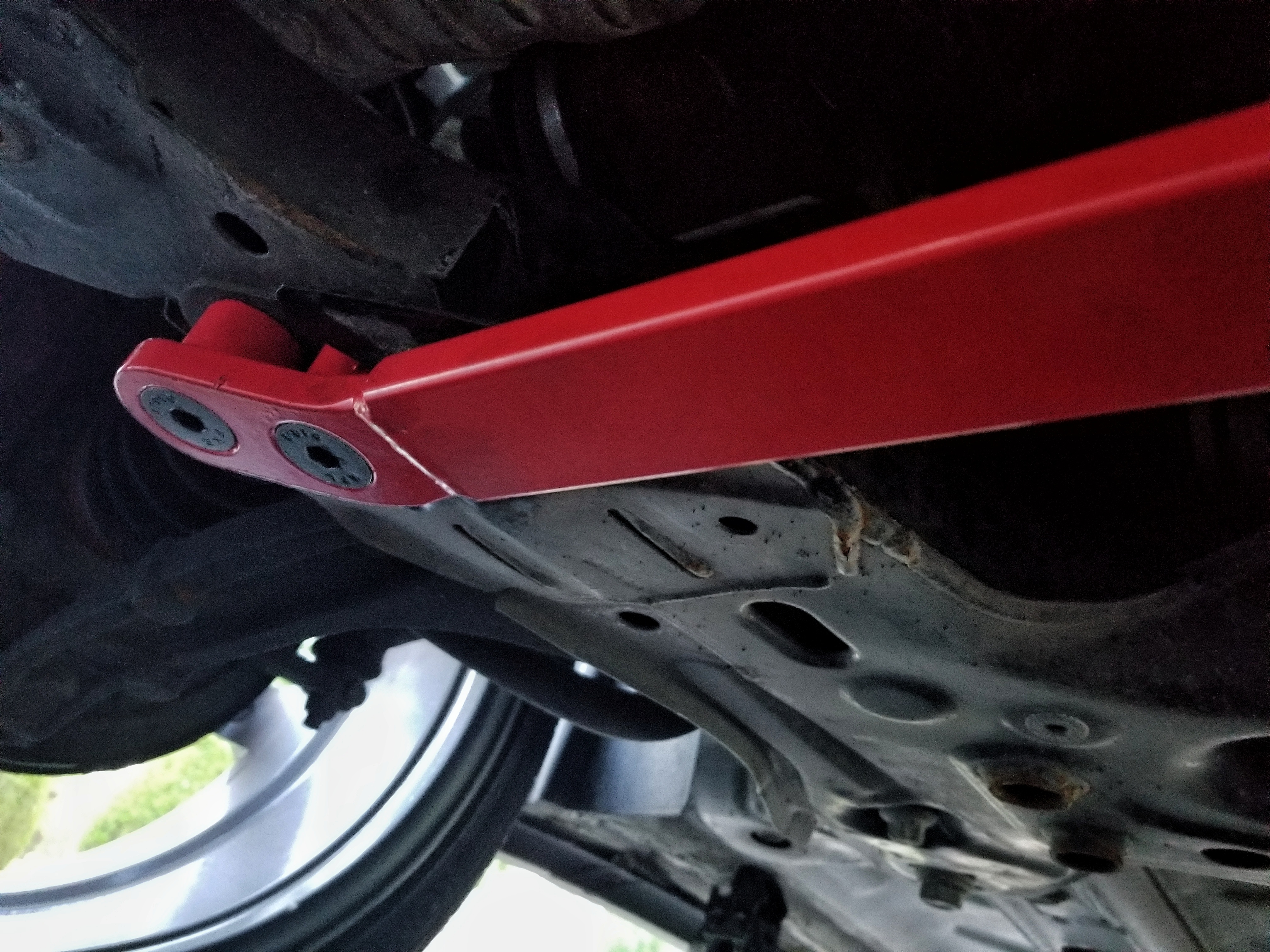 The passenger's side underside view of a red Corsa Forza V1 lower subframe brace mounted on a 2013 Fiat 500 Abarth