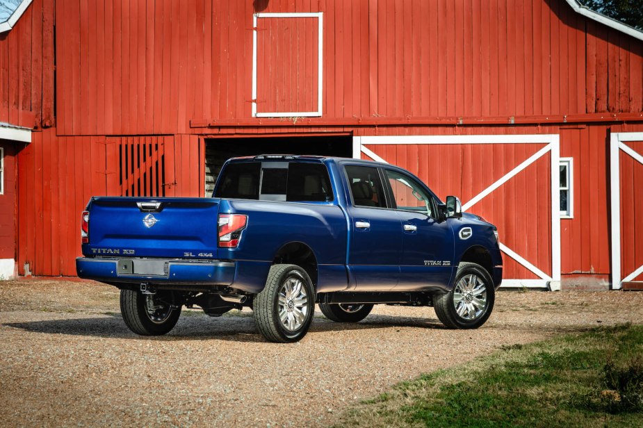 Blue, medium duty Nissan Titan XD parked in front of a bright, red barn.