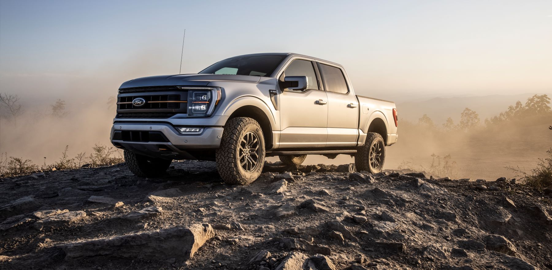 2021 Ford F-150 Tremor full-size pickup truck parked on a rocky mound surrounded by dust clouds