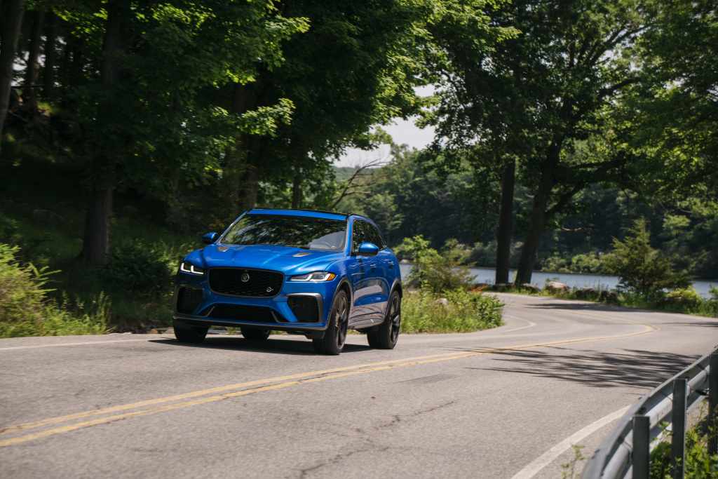 A blue Jaguar F-Pace on a road by a lake