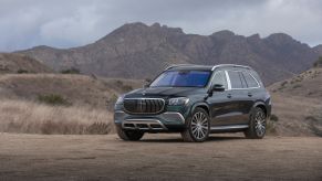 A 2021 Mercedes-Maybach GLS luxury SUV model parked on a sandy plain near rolling hills of rock and grass