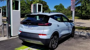 The rear 3/4 view of a light-blue 2022 Chevrolet Bolt EUV at a green-white Electrify America charging station