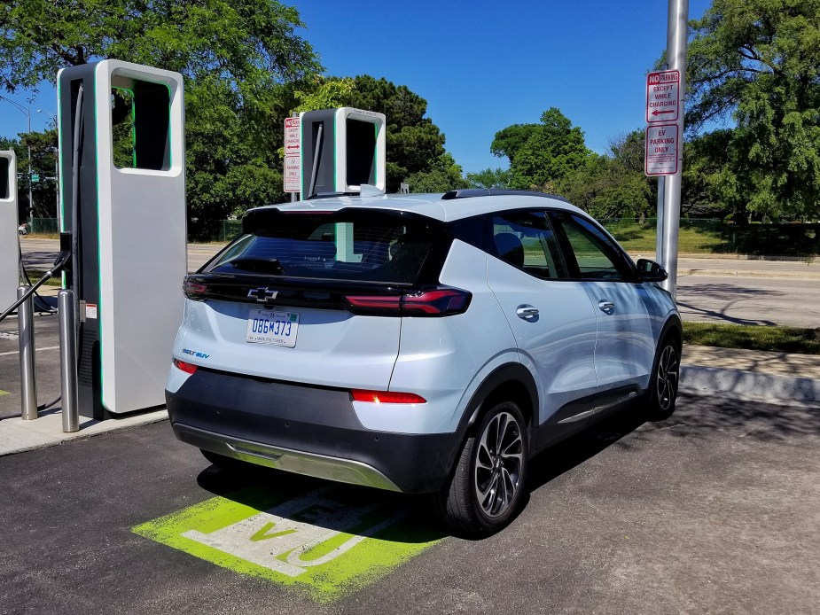 The rear 3/4 view of a light-blue 2022 Chevrolet Bolt EUV at a green-white Electrify America charging station