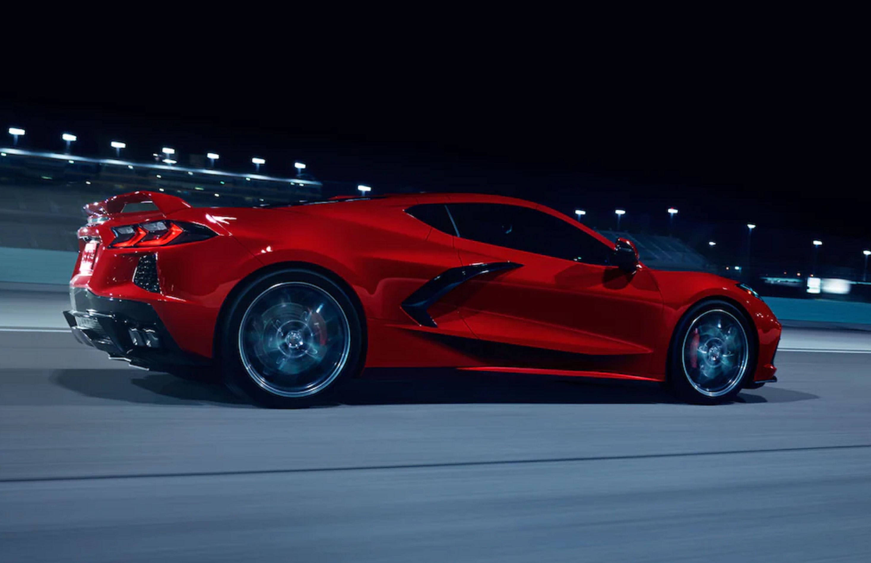 The rear 3/4 view of a red 2022 Chevrolet C8 Corvette 3LT Coupe Z51 driving on a racetrack at night
