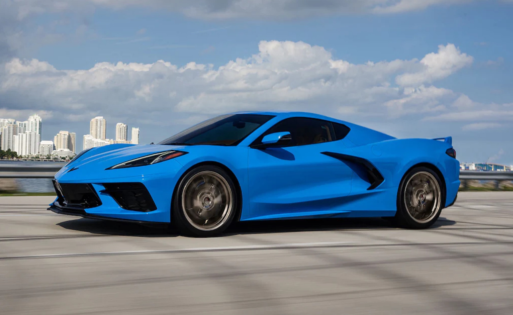 A blue 2022 Chevrolet C8 Corvette 3LT Coupe driving down a city road by a body of water