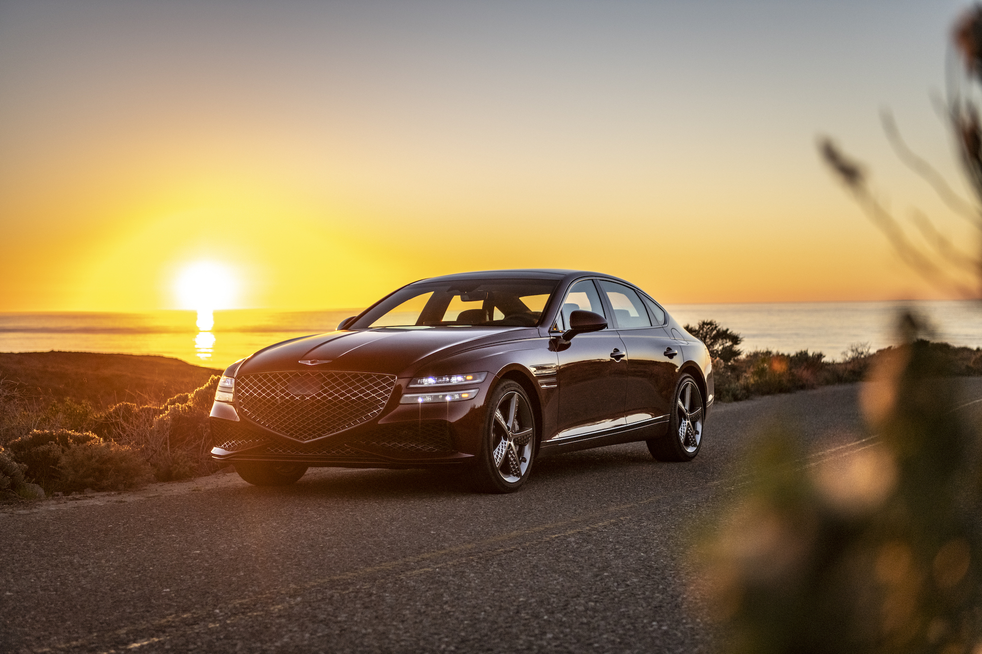 A 2022 Genesis G80 luxury sedan parked on the side of the road as the sun sets behind it