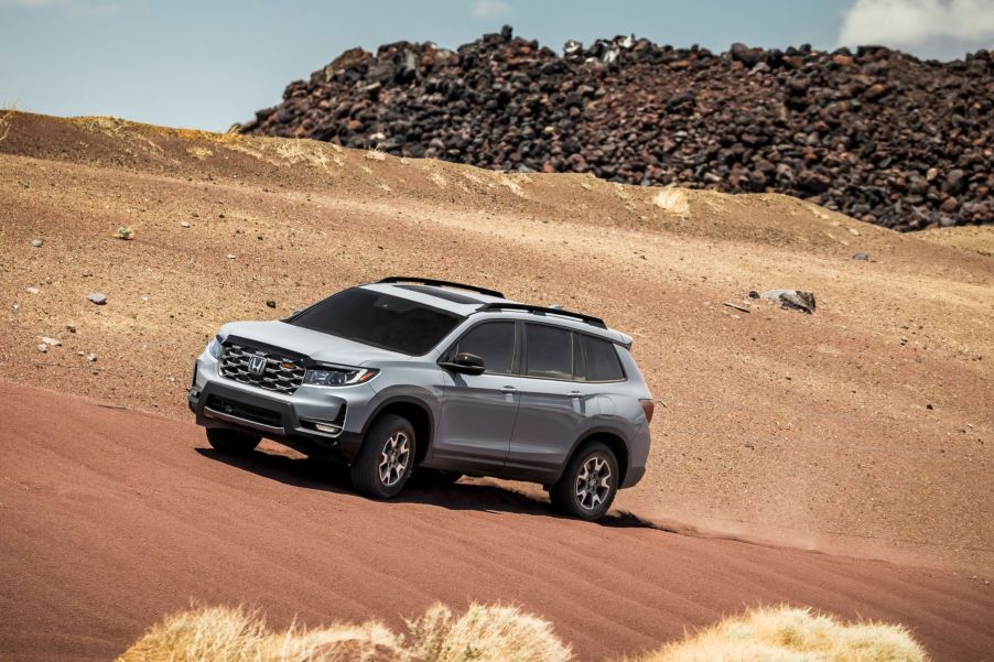 A gray 2022 Honda Passport TrailSport driving on a dirt desert dune near a large pile of garbage