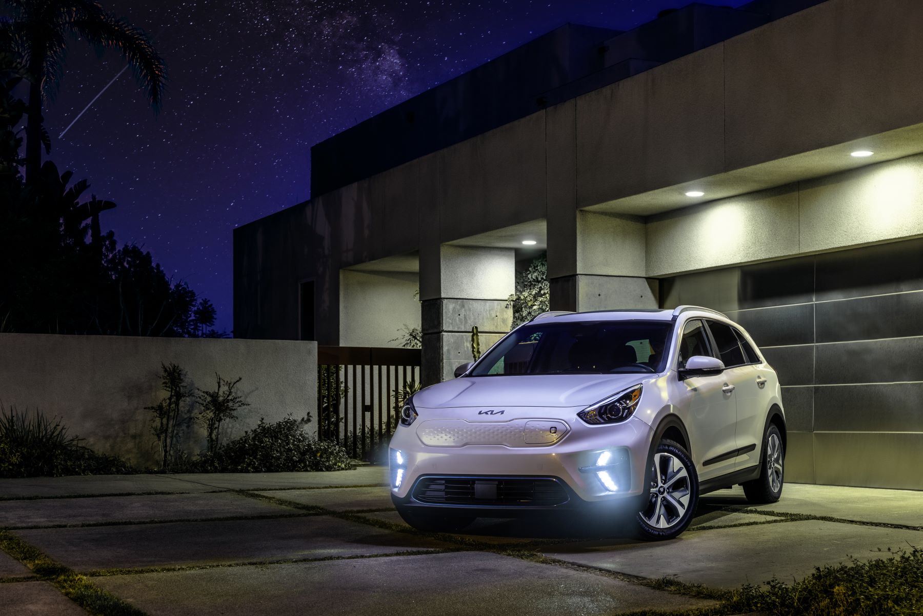 A white 2022 Kia Niro EV parked outside a garage at night with its headlights on