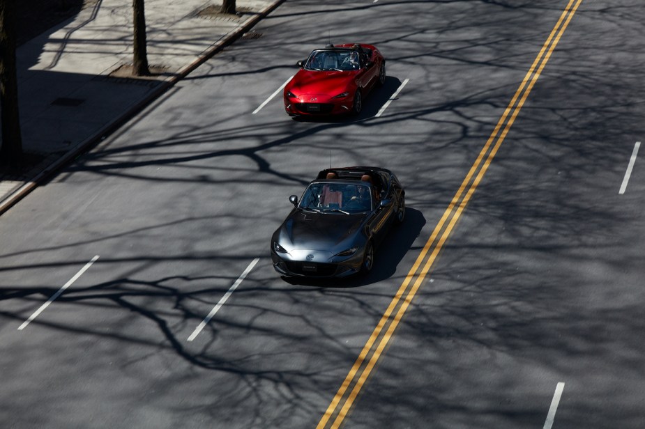 A pair of Mazda MX-5 Miatas driving down the road.