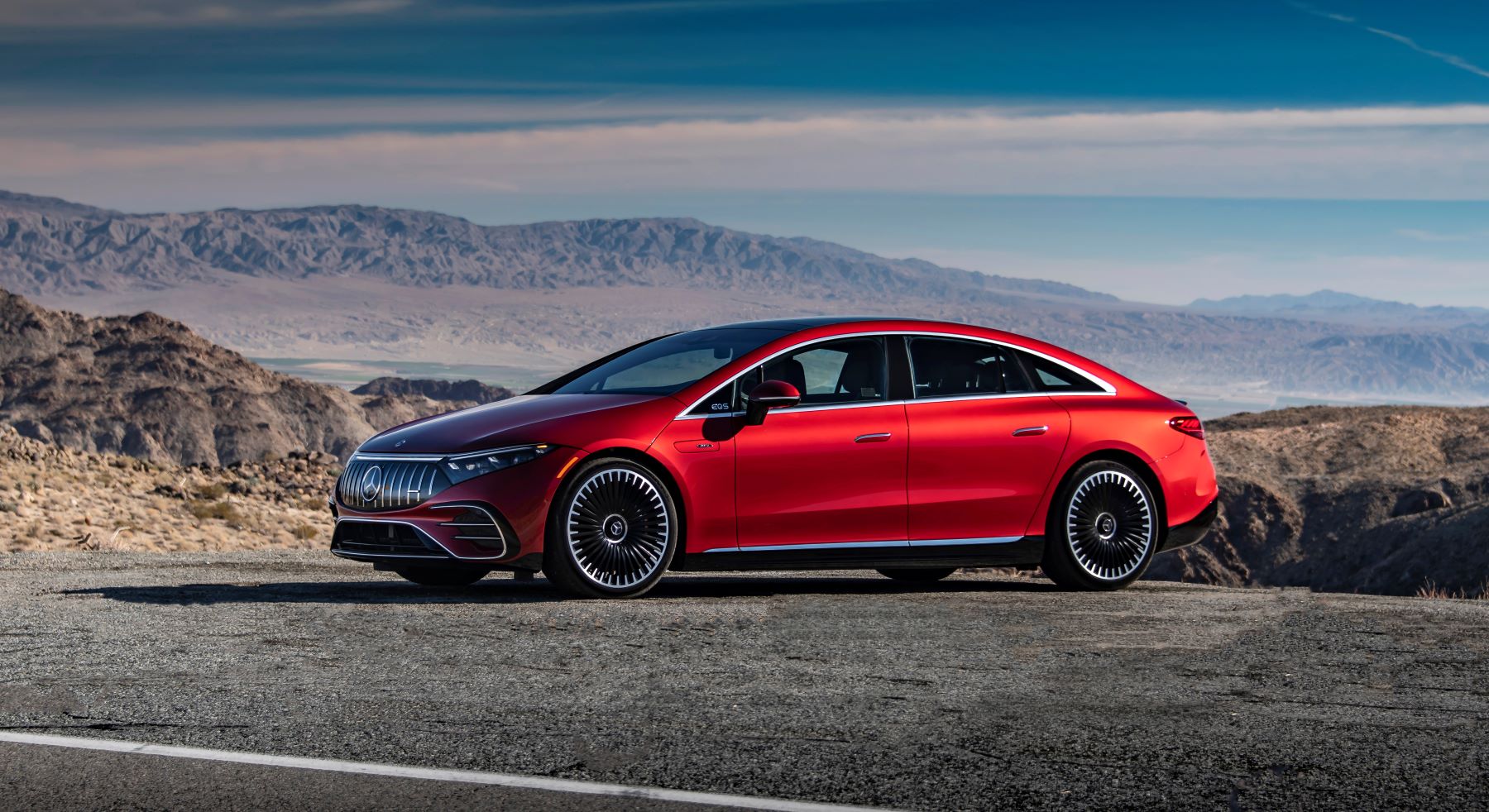 A red 2022 Mercedes-Benz AMG EQS all-electric luxury sports car sedan parked on the side of a highway road near the sea