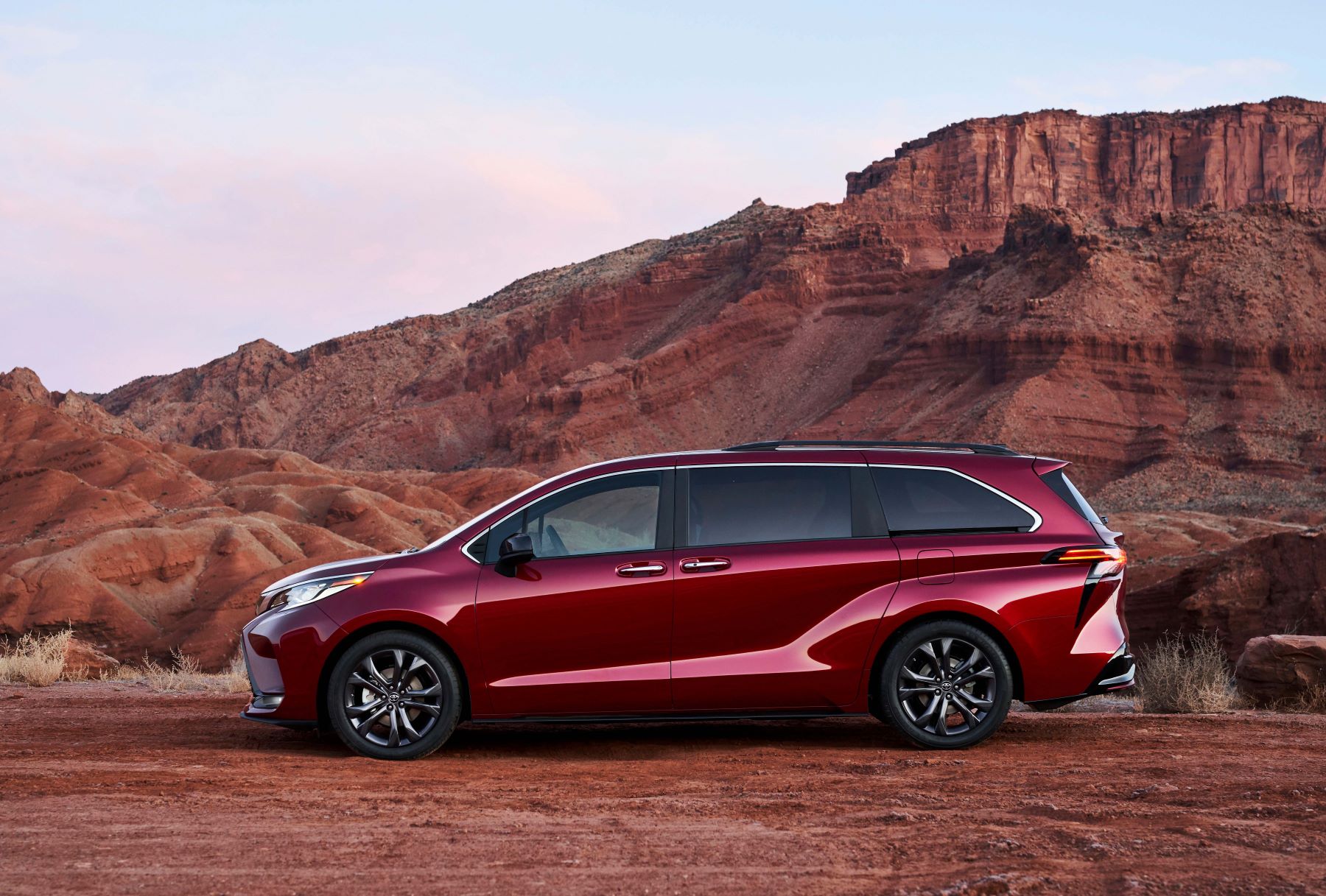 A 2022 Toyota Sienna minivan in Ruby Flare Pearl parked near orange mountains cliffs in the desert