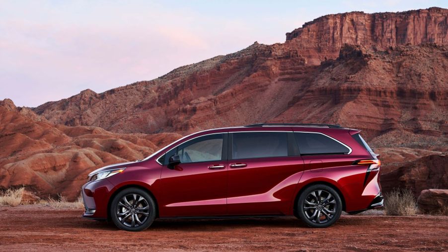 A 2022 Toyota Sienna minivan in Ruby Flare Pearl parked near orange mountains cliffs in the desert