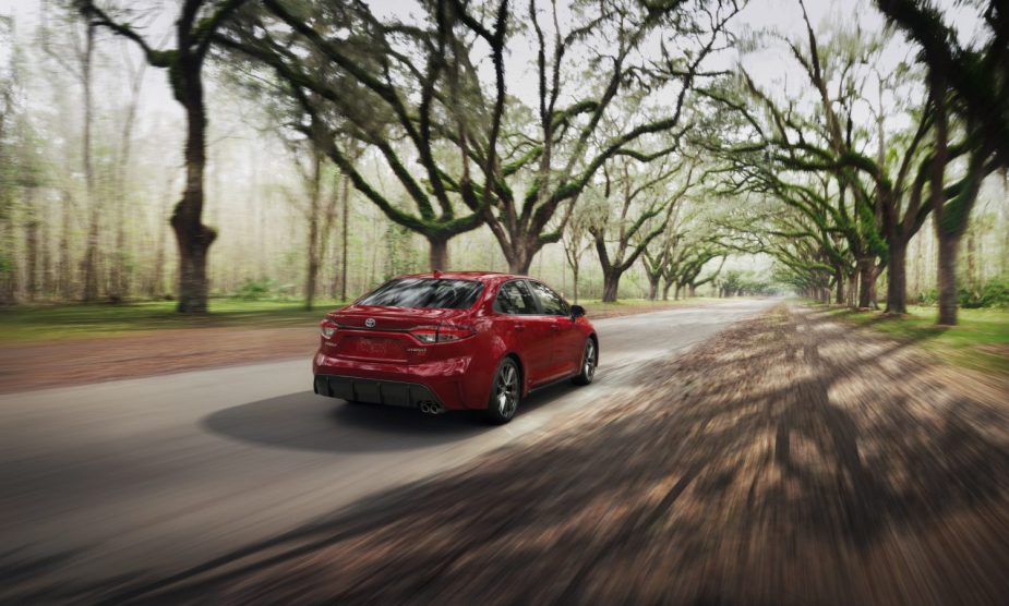 A red 2022 Toyota Corolla Hybrid drives down a back road.