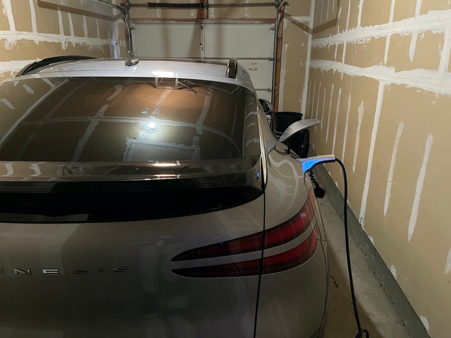 The 2023 Genesis GV60 plugged into the household wall outlet.