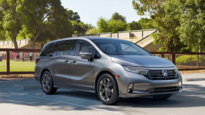A silver gray 2023 Honda Odyssey minivan parked near a sports field where children are playing soccer