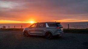 A 2023 Kia Carnival MPV/minivan parked near the water as the sunsets over the sea