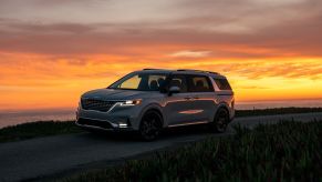 A gray 2023 Kia Carnival minivan/MPV parked on a trail near the ocean at sunset