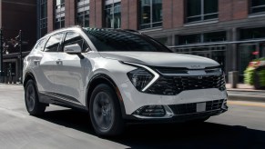 A white 2023 Kia Sportage hybrid SUV is driving on the road.