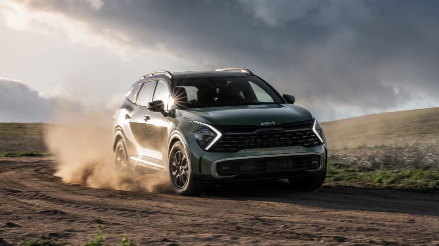 A green 2023 Kia Sportage X-Pro compact SUV driving on a dirt road as its tires kick up dust clouds