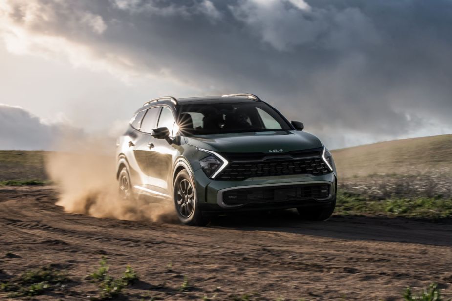 A green 2023 Kia Sportage X-Pro compact SUV driving on a dirt road as its tires kick up dust clouds
