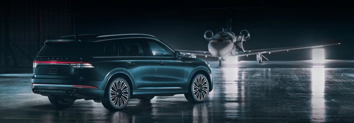 Green 2023 Lincoln Aviator Black Label Grand Touring on a runway near a private jet. The Lincoln Aviator is one of the best three-row plug-in hybrids to buy.