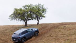 A 2023 Mazda CX-50 compact crossover SUV model climbing a grass hill on a dirt road