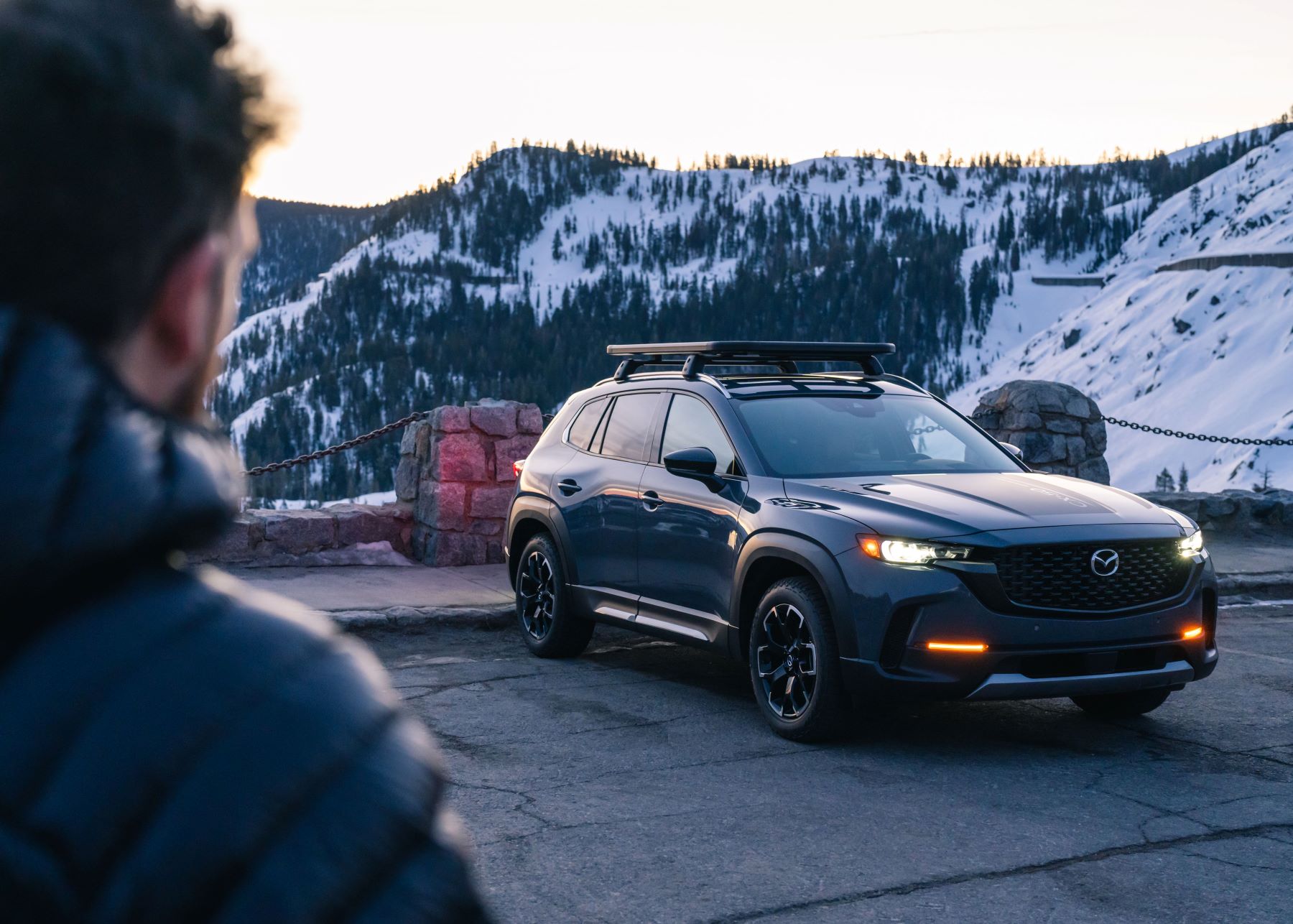 A 2023 Mazda CX-50 compact crossover SUV model parked on a cracked asphalt lot in snowy forest mountains