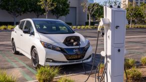 A white 2023 Nissan Leaf S electric hatchback plugged-in at a charging station