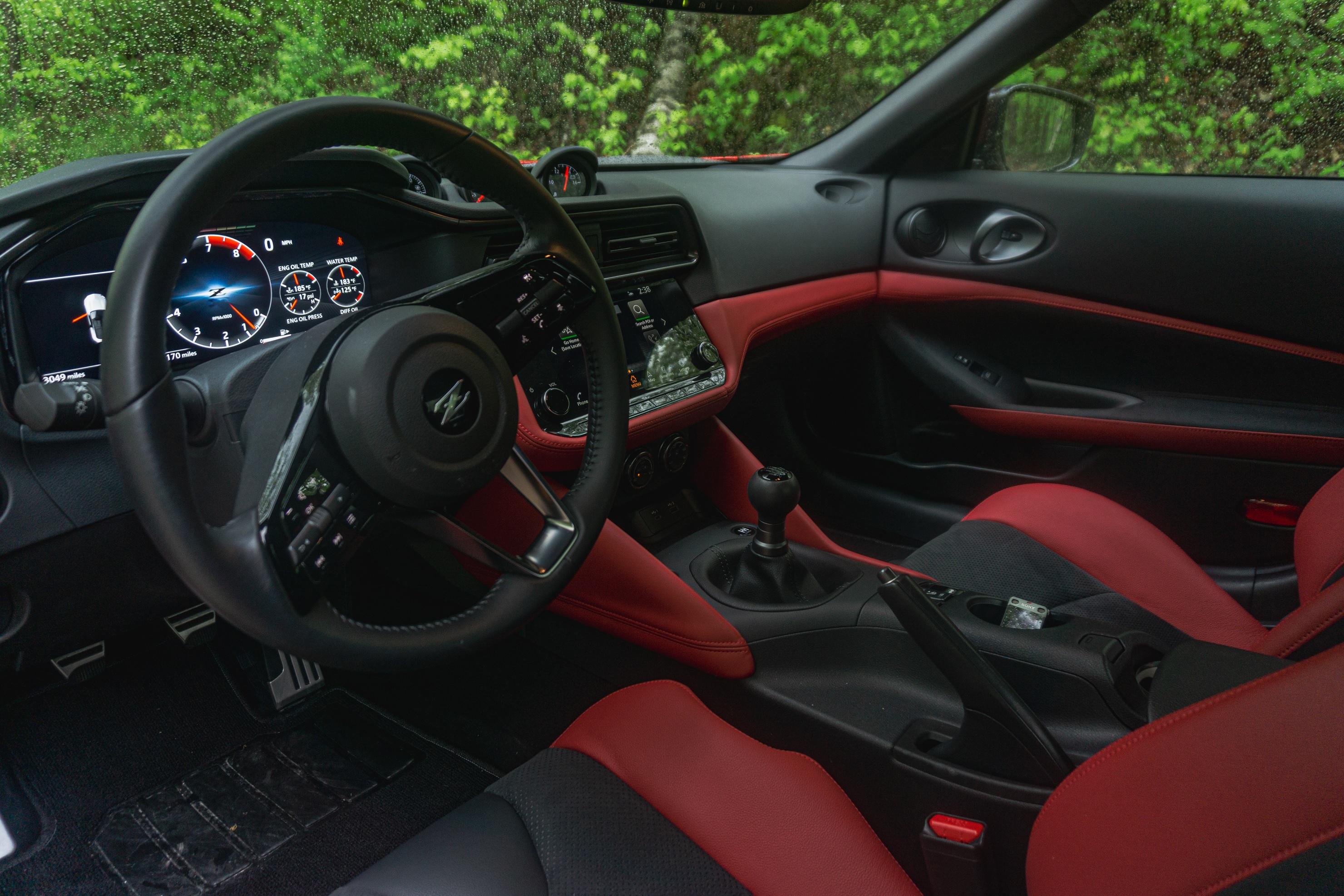 The red-and-black leather seats and dashboard of a 2023 Nissan Z Performance on a forest road