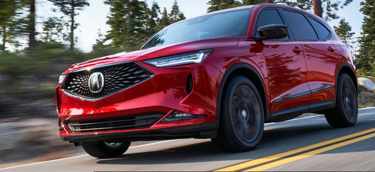 A red 2022 Acura MDX driving down a wooded road.