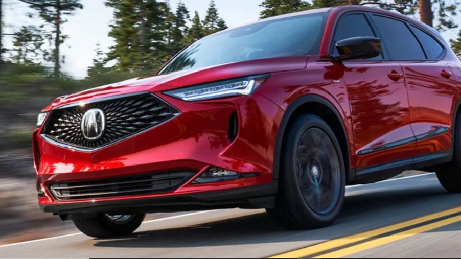 A red 2022 Acura MDX driving down a wooded road.