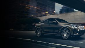 A beige 2022 BMW X6 driving through the city.