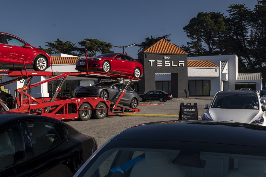 Truck and parking lot showing the limited inventory of a car dealership, Tesla sign visible in the background.