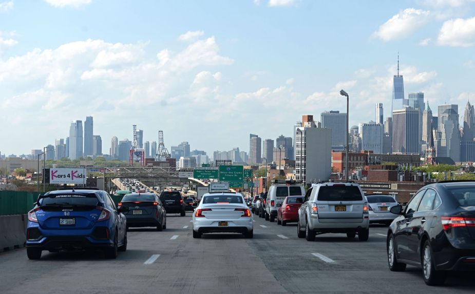 A standstill traffic jam on an expressway, the skyline of New York City visible in the background.