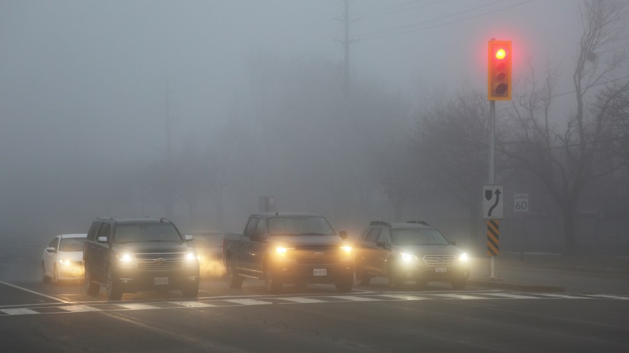 Cars driving in fog with their headlights on.