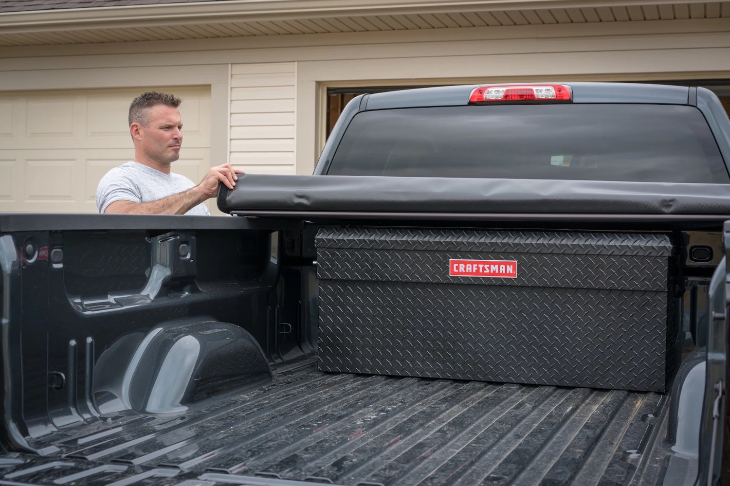 Man rolling up the tonneau cover on his pickup truck to reveal a Craftsman vault-style locking tool chest in the bed.