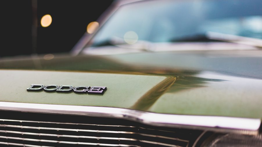 Closeup of the Dodge logo on a classic green muscle car, the chrome of its grille just visible in the foreground.