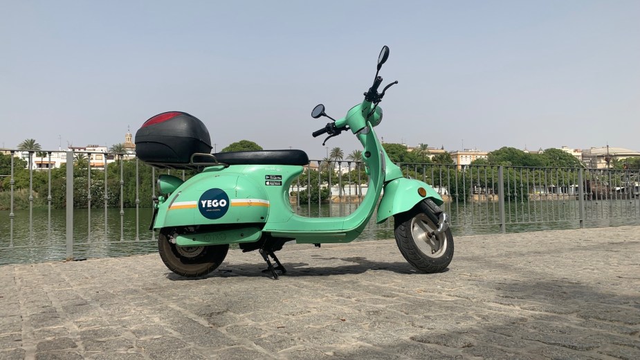 YEGO rental scooter on its kickstand, on a cobbled street by a river.