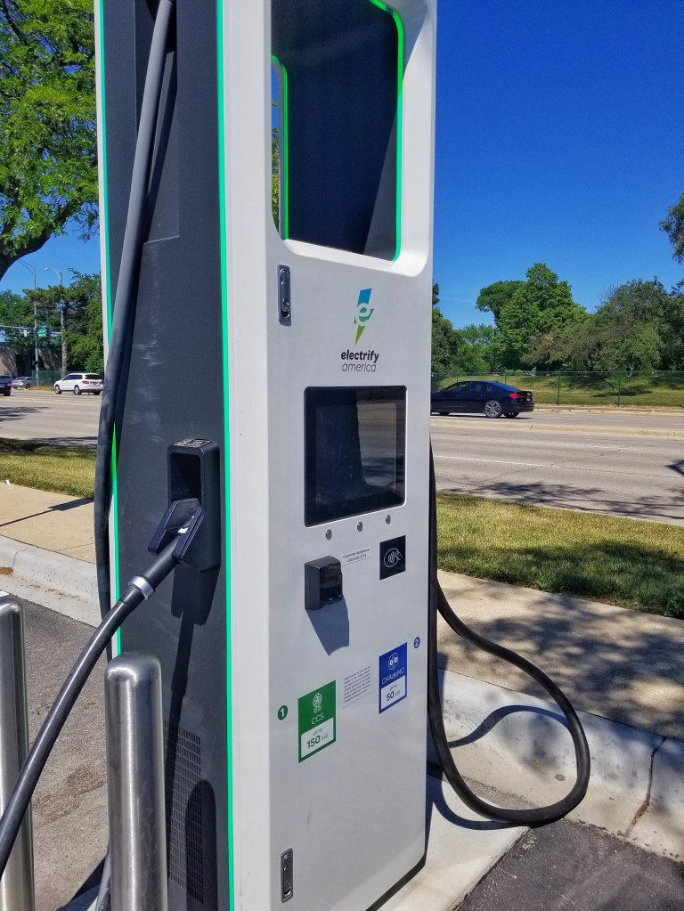 A white-gray-and-green Electrify America charging station in a shopping mall parking lot