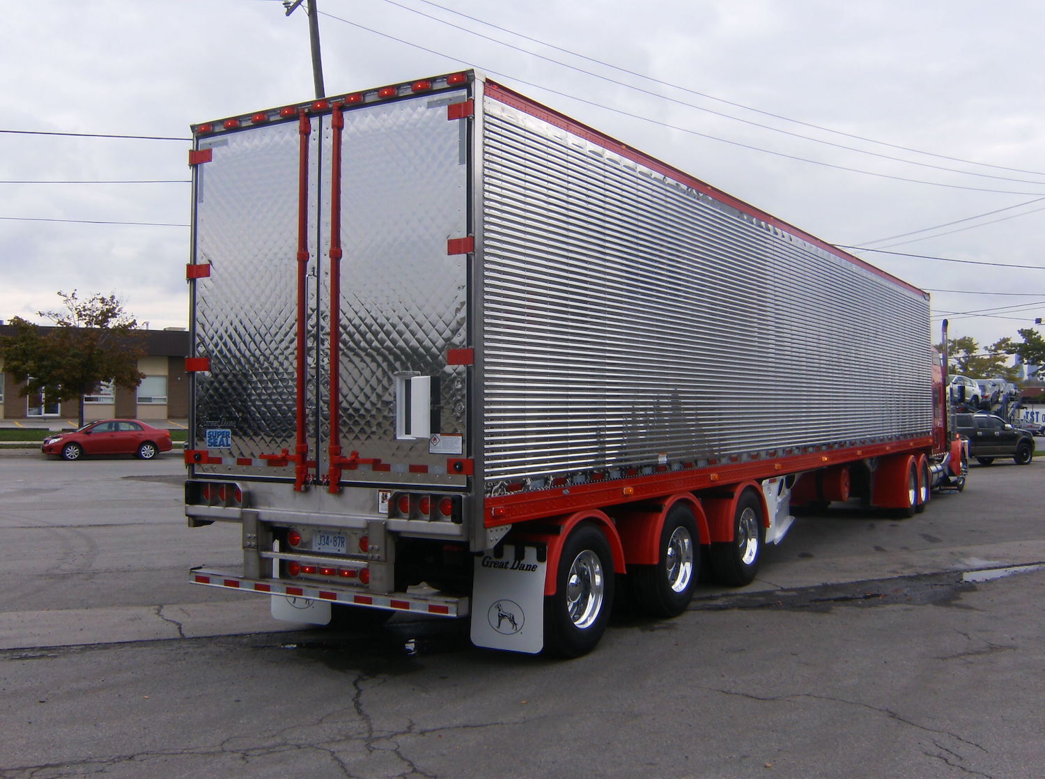 A refrigerated semi truck trailer with an open rear vent door, the truck tractor and a street visible in the background.