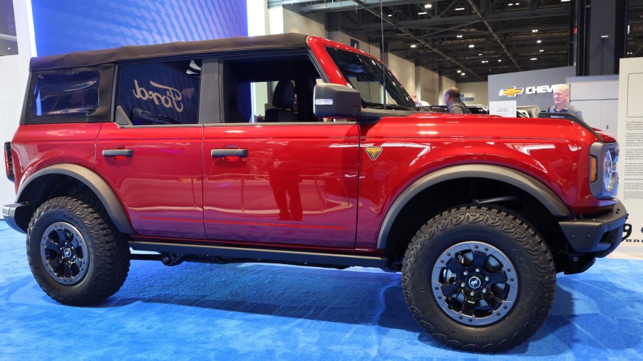 One of the red new Ford Bronco models on a blue floor parked indoors in front of a purple background.