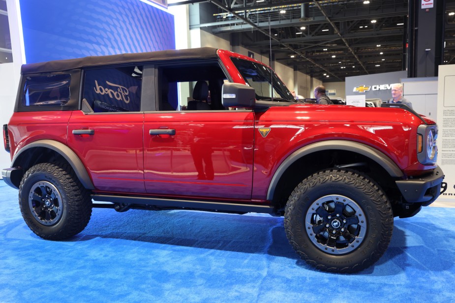 One of the red new Ford Bronco models  on a blue floor parked indoors in front of a purple background. 