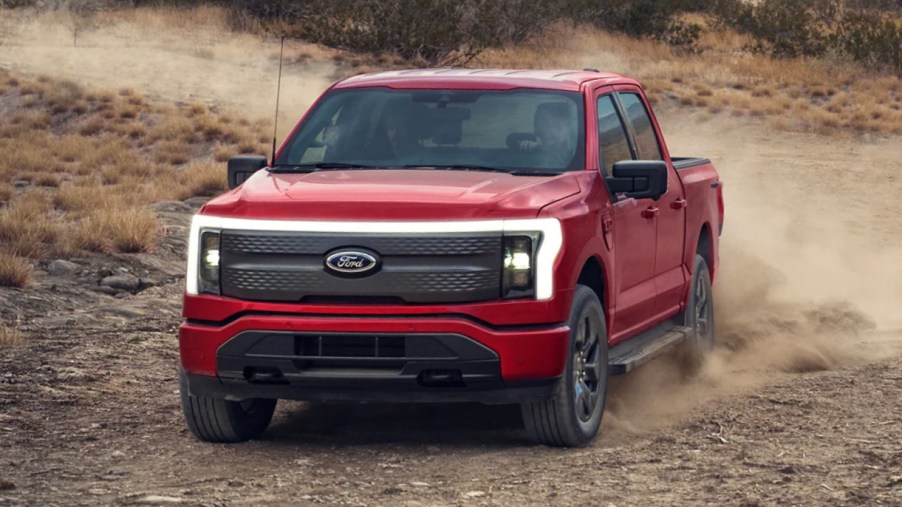 A red Ford F-150 Lightning electric pickup truck is driving off-road.
