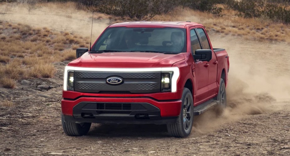 A red Ford F-150 Lightning electric pickup truck is driving off-road. 