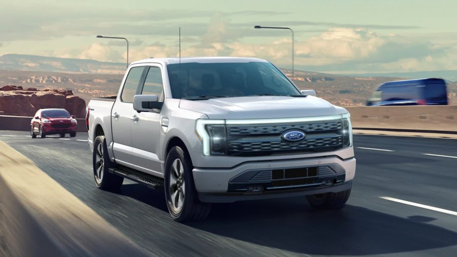 A gray 2022 Ford F-150 Lightning electric pickup truck is driving on the road.