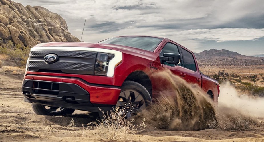 A red Ford F-150 Lightning electric pickup truck is driving off-road. 