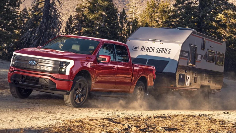 A red 2022 Ford F-150 Lightning electric pickup truck is towing an RV.