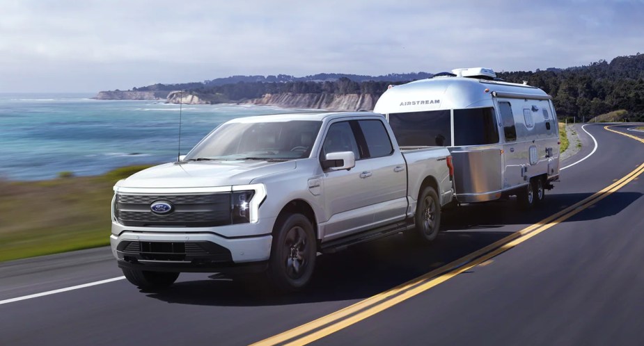 A white Ford F-150 Lightning electric pickup truck is towing a trailer.