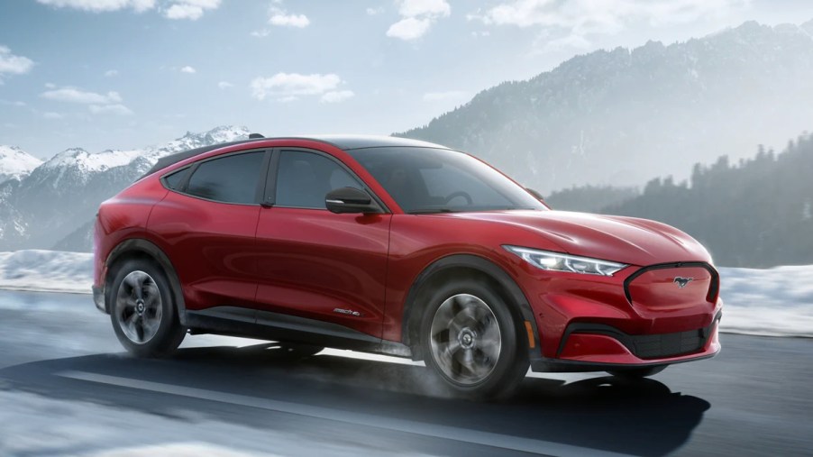 A red Ford Mustang Mach-E electric SUV is driving on the road.