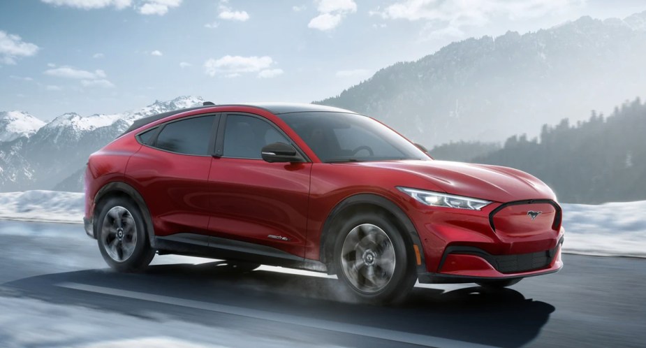 A red Ford Mustang Mach-E electric SUV is driving on the road. 